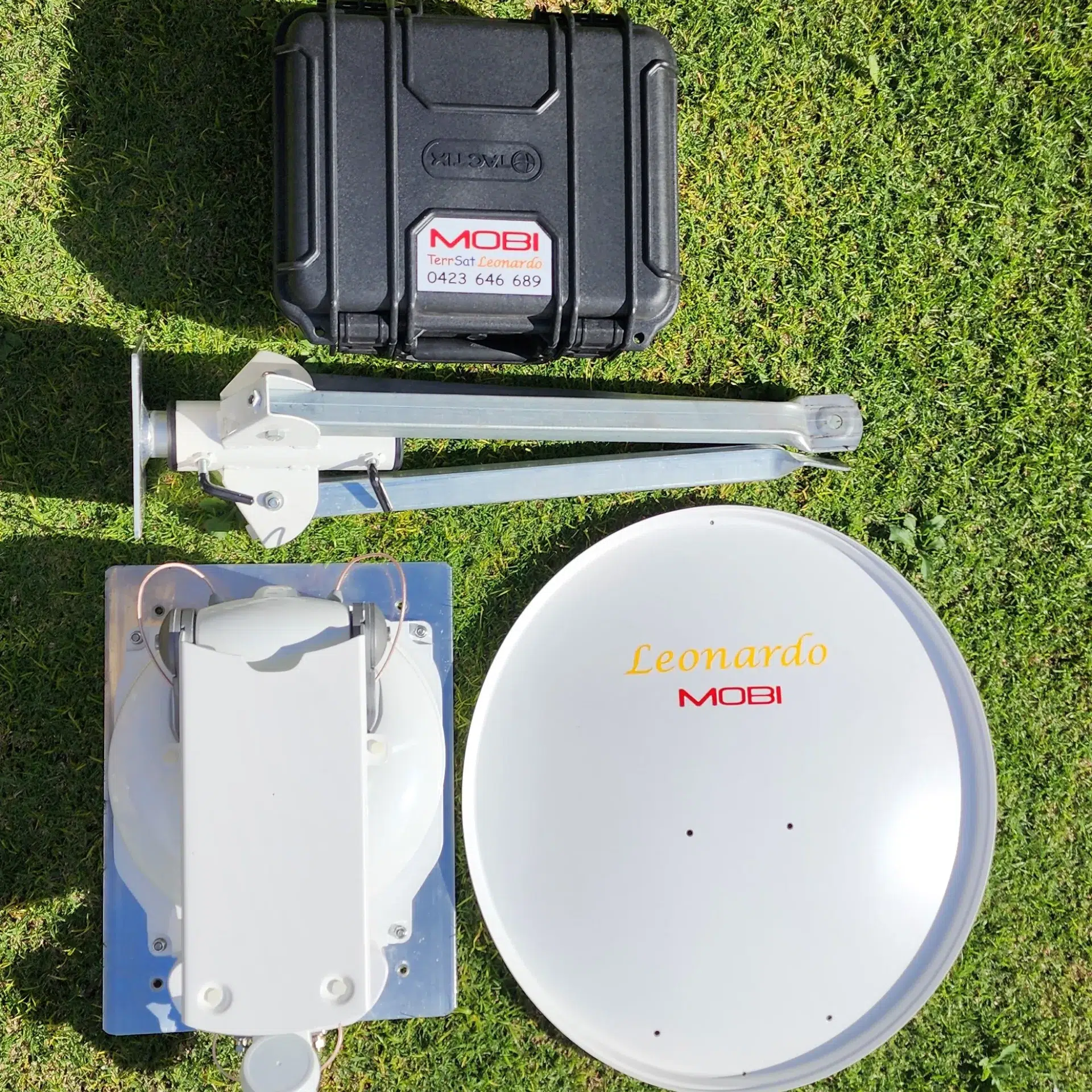 A photo of some equipment on grass, specifically a suitcase and a dis-assembled antenna.
